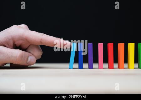Foto concettuale di una mano che inizia una reazione a catena con dominazioni colorate. Effetto domino con pietre colorate e copyspace. Foto Stock