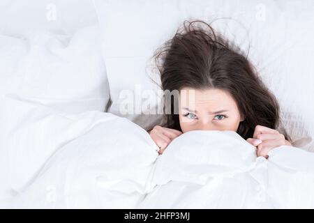 La ragazza strisciò sotto il velo con il suo corpo, solo la testa è visibile. La brunetta si trova a letto, riscaldandosi una mattina d'inverno. Svegliarsi lontano Foto Stock