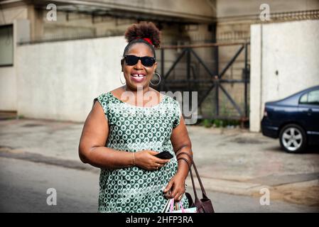 bella donna matura affari felice indossando occhiali da sole e sorridendo per strada. Foto Stock