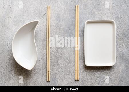 Piatti bianchi vuoti e bacchette di bambù su sfondo grigio con spazio di copia Foto Stock