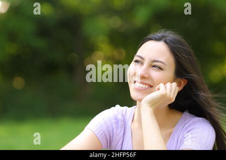 Donna asiatica felice che pensa guardando il lato in un parco Foto Stock