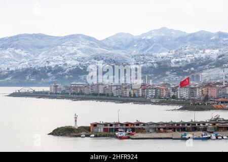 Vista sulla costa con torre faro bianca e bandiera turca all'ingresso del piccolo porto di pescatori di Arakli, Trabzon, Turchia. Paesaggio della costa del Mar Nero Foto Stock
