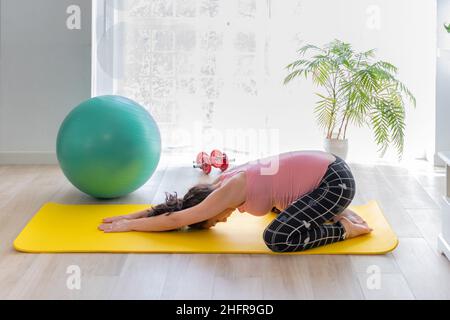 giovane donna incinta sdraiata su materassino di esercizio facendo indietro stretching a casa.concetto di assistenza sanitaria e sport in gravidanza e gestazione Foto Stock