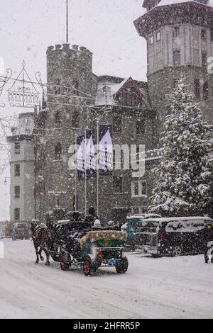 St Moritz, Svizzera - Dicembre 08 2021: Carrozza trainata da cavalli porta il turista di fronte al famoso palazzo di Badrutt nel villaggio di Saint Moritz nel Th Foto Stock