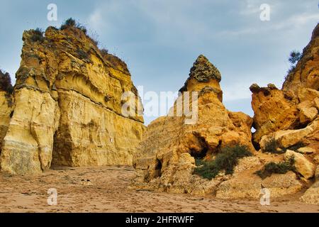 Formazioni rocciose giallo-rosse, erose in forme frastagliate, si innalzano dalla sabbia. Lagos, Algarve, Portogallo Foto Stock