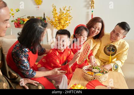 Famiglia felice gustando noci e frutta candita con tè quando festeggia il Capodanno lunare a casa Foto Stock