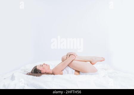 La brunetta conduce uno stile di vita sano. Una ragazza si sveglia al mattino, facendo yoga a letto, facendo stretching. Camera bianca. Esercizio al mattino. H Foto Stock