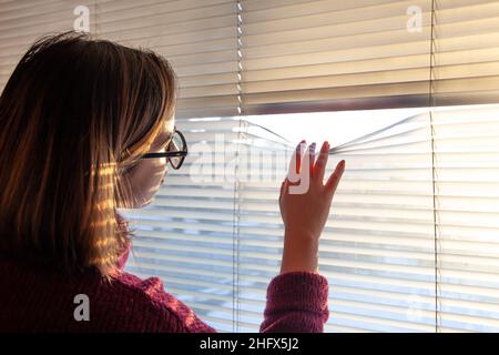 Una donna guarda attraverso i bui alla luce del sole del mattino presto. Foto Stock