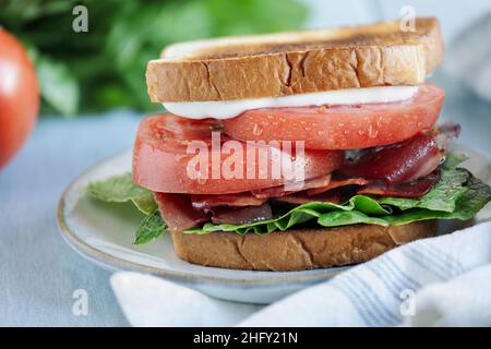 Panino fatto in casa con pancetta, lattuga e pomodoro su un tavolo bianco rustico. Messa a fuoco selettiva con sfondo sfocato in primo piano. Foto Stock