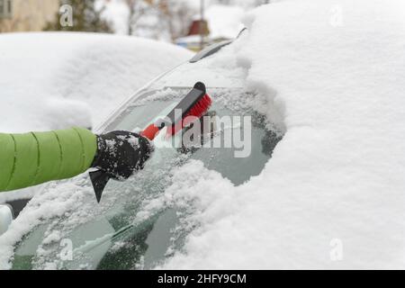 Mano di uomo con una spazzola che pulisce la neve dalla vettura in inverno dopo la nevicata Foto Stock