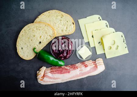 BlackBerry Bacon ingredienti di sandwich al formaggio alla griglia: Vista dall'alto del pane alla pasta madre, pancetta cruda e altri ingredienti su sfondo scuro Foto Stock