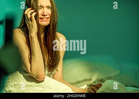 Depressione. Ottieni le cattive notizie. Smettiti. Una donna con un volto sporco da mascara si siede a letto e piange, parlando al telefono. Heartbroken. Per soffrire. B Foto Stock