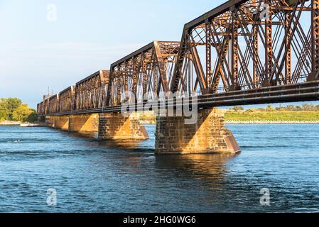 Vista di un ponte ferroviario arrugginito vuoto attraverso un fiume al tramonto Foto Stock