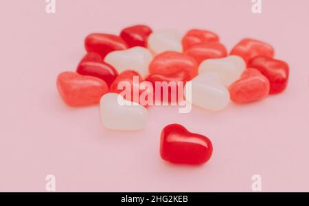 Una manciata di caramelle di zucchero colorate a forma di cuore su sfondo rosa Foto Stock