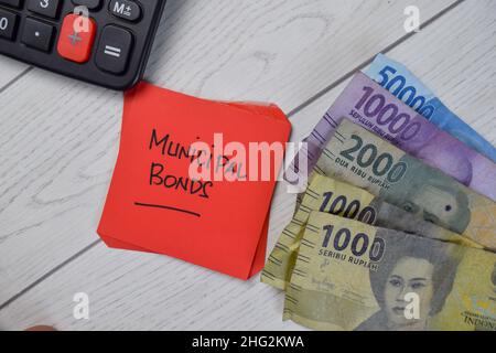 Le obbligazioni comunali e la valuta indonesiana scrivono su note adesive isolate su tavola di legno. Foto Stock