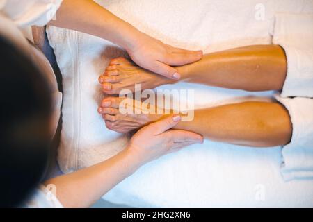 Vista dall'alto delle mani della massaggiatrice che offre un massaggio essenziale con olio alle gambe di una donna in un salone spa. Primo piano verticale. Cura del corpo Spa. Cura della pelle di bellezza. Foto Stock