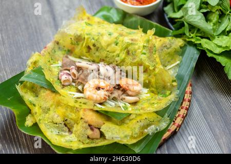 Banh Xeo è una tradizionale torta vietnamita. Gli ingredienti della torta includono farina, gamberi, maiale, tuberi attorcigliati, calamari... e verdure per accompagnare il cak Foto Stock