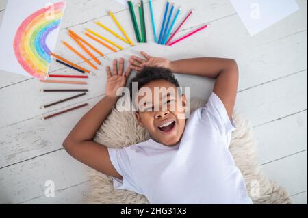 Vista dall'alto del ragazzo allegro che giace sul pavimento Foto Stock