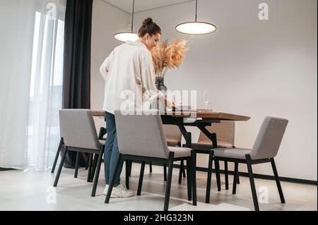 Giovane donna in una camicia bianca che mette le piastre sul tavolo Foto Stock