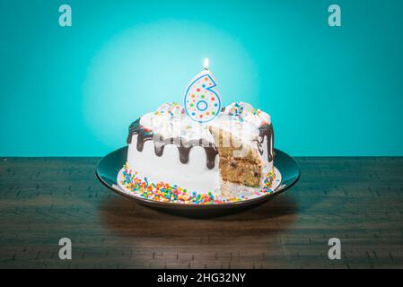 Una torta di compleanno, mancante di una fetta, porta una candela nella forma del numero 6. Foto Stock