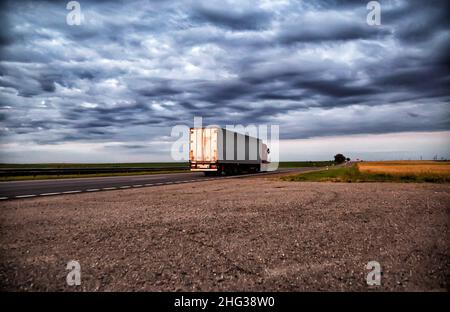 Un camion con un frigorifero per trasportare un carico deperibile su un'autostrada sullo sfondo di un cielo nuvoloso e nuvole. Foto Stock