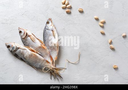 Carpa salata ed essiccata. Pesce legato con spago, e pistacchi sparsi su un fondo di cemento chiaro con spazio copia. Tradizionale birra snack. Vista dall'alto Foto Stock