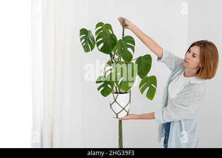 Appendiabiti di piante di macramo verde fatti a mano con la pianta in vaso sono appesi sulla mano della donna. Vaso e pianta della monstera Foto Stock