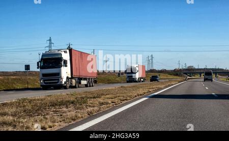 Un convoglio di due autocarri con rimorchi per container trasporta container pesanti dal porto marittimo. Il concetto di società logistiche che trasportano merci da Foto Stock