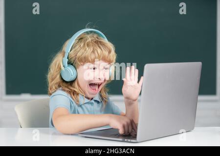 Ragazzo divertente in cuffie studiare online, bambino in auricolari prendere Internet web lezione. Emozioni stupite per i bambini. Foto Stock