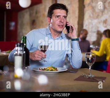 Uomo felice che parla al telefono durante il pasto serale Foto Stock