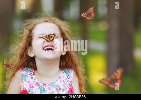 Divertente ragazza ridente ricciola con una farfalla sul naso. Sorriso sano con denti bianchi. Concetto di respirazione libera. Foto Stock