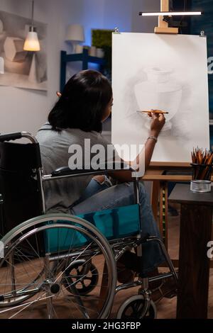 Giovane donna artista con disabilità disegno vaso su tela con disegno matita grafica. Studente in sedia a rotelle che lavora all'illustrazione di disegno usando gli strumenti di pittura per la lezione d'arte in atelier domestico Foto Stock