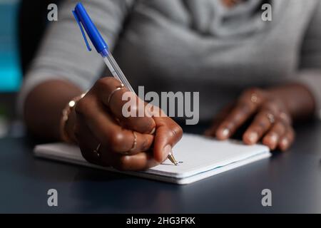 Primo piano della mano che tiene la penna per scrivere sul file del libro di testo, lavorando da casa sul progetto di affari. Persona che utilizza il notebook per prendere appunti e scrivere informazioni su carta. Lavoro remoto alla scrivania Foto Stock