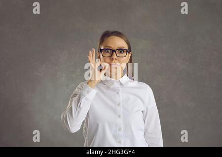 Giovane donna con gli occhi ampiamente aperti mostrando il gesto chiedendo di mantenere il silenzio Foto Stock