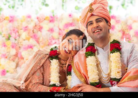 Ritratto di una felice coppia di nozze indiana seduta insieme su mandap Foto Stock