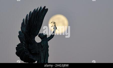 Brighton UK 18th gennaio 2022 - la Luna del lupo affonda dietro la Statua della Pace di Brighton all'inizio di questa mattina . Tradizionalmente la prima luna piena dell'anno è conosciuta come la Luna del lupo . Credit Simon Dack / Alamy Live News Foto Stock