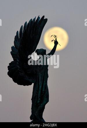 Brighton UK 18th gennaio 2022 - la Luna del lupo affonda dietro la Statua della Pace di Brighton all'inizio di questa mattina . Tradizionalmente la prima luna piena dell'anno è conosciuta come la Luna del lupo . Credit Simon Dack / Alamy Live News Foto Stock
