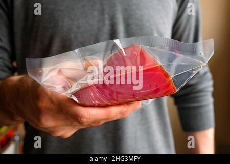 Tiene in mano un pezzo di tonno in una confezione. Foto Stock