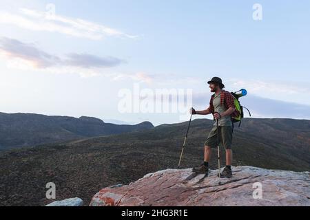 Intera lunghezza di giovane escursionista caucasico maschio con pali in piedi sulla cima della montagna Foto Stock