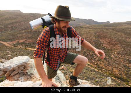 Bearded giovane maschio escursionista caucasico arrampicata picco roccioso di montagna al tramonto Foto Stock