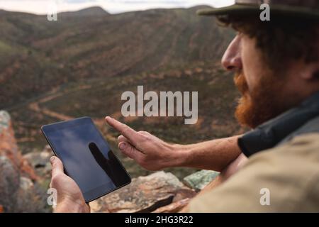 Giovane avventuriero caucasico maschio utilizzando tablet digitale sulla cima della montagna Foto Stock