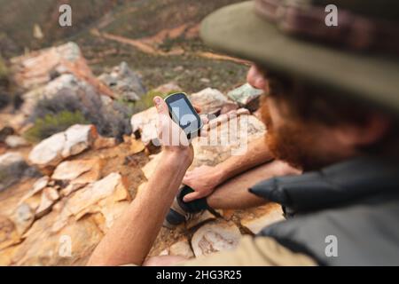 Giovane avventuriero caucasico maschio utilizzando smartphone mentre si siede sulla cima della montagna Foto Stock