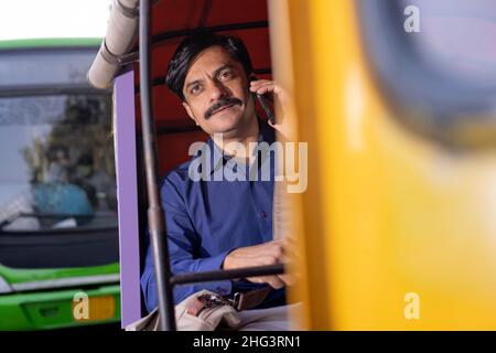 Uomo che parla sullo smartphone mentre si va in ufficio da Auto Rickshaw Foto Stock