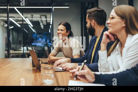 Felice donna d'affari ridendo mentre conduce un incontro con i suoi colleghi. Gruppo di uomini d'affari diversi che lavorano insieme in un ambiente di lavoro moderno. Busi Foto Stock