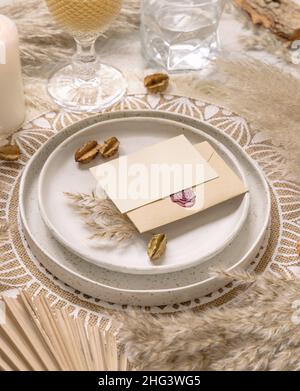 Tavolo da nozze posto sul placemat bohémien con carta vuota orizzontale primo piano. Boho mockup carta da matrimonio. Sagoma beige tropicale con piante secche, pa Foto Stock