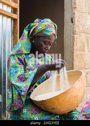 Senegal, Africa - Jan, 2019: Ritratto di una bella donna senegalese in costume tradizionale chiamato 'boubou' con una ciotola di riso Foto Stock