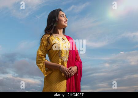 Donna felice in salwar giallo in piedi sotto il cielo blu Foto Stock