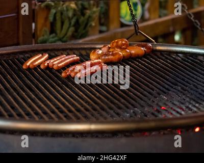 Appetitose e deliziose salsicce si trovano sulla griglia di una padella al buio. Da sotto la griglia, le calici calde bruciano. Rinfreschi all'aperto di festa in città. Foto Stock