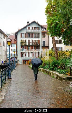 L'uomo cammina con un ombrello nero in una strada di Annecy, alta Savoia, Francia, sotto un giorno di pioggia di autunno Foto Stock