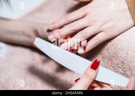 Immagine ravvicinata del processo manicure, manicurista che usa la lima del chiodo sulle unghie femminili. Attenzione all'unghia. Foto Stock